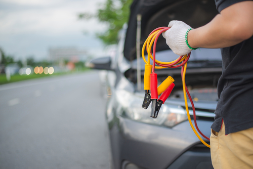 Young man charging battery car with electricity trough jumper cables on the country road,copy space.insurance and service concept. Young man charging battery car with electricity trough jumper cables on the country road,copy space.insurance and service concept.